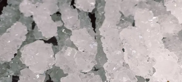 Düzensiz şekilli, şeffaf beyaz kaya şekeri kristallerinin makro çekimi dokusunu ve ışıltılı görünümünü gösteriyor..