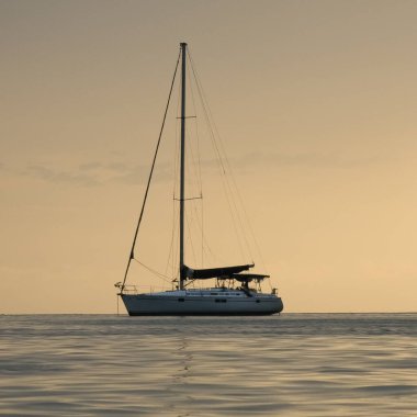 Altın bir günbatımında sakin sulara demir atmış sakin bir yelkenli. Geminin silueti, göğün ılık tonlarına karşı huzurlu ve huzurlu bir manzara yaratır..