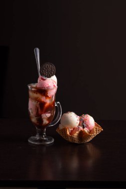 Çikolatalı kurabiyeyle doldurulmuş ve sosla ıslatılmış bir bardakla yanında dondurma kepçeleri olan bir kurabiye bardağı..