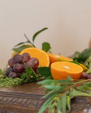 Üzüm, portakal ve yeşil yapraklardan oluşan canlı bir düzenleme beyaz bir arka plana karşı ahşap bir masaya yerleştirilmiş, doğal ve taze temalı görseller için mükemmel..