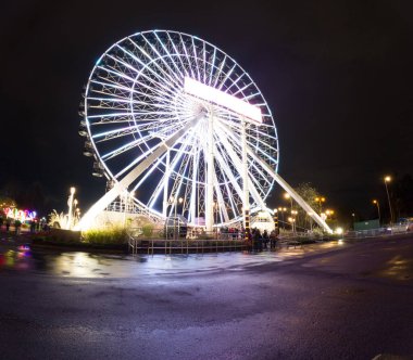 Geceleri dönme dolap, aşağıdaki ıslak zemine renkli ışıklar saçar..