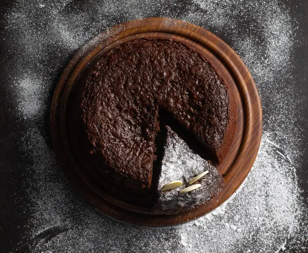 Tahta bir tabakta zengin, nemli bir çikolatalı pastanın yukarıdan görünüşü, dilimlenmiş ve toz haline getirilmiş şeker ile.
