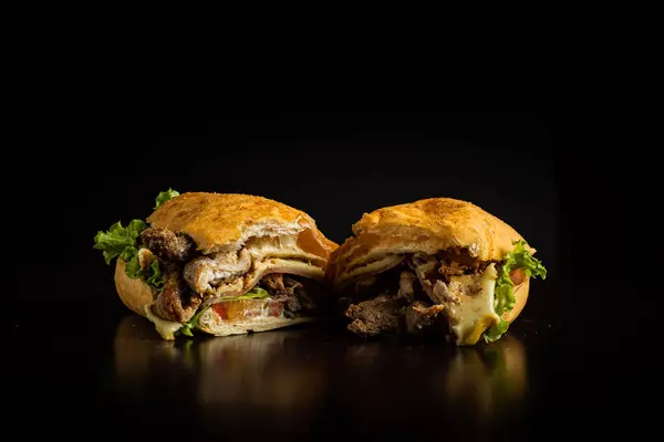 Çıtır ekmekli sandviçler, tavuk, peynir, domates ve marul parçaları, ikiye bölünmüş ve siyah arka planda sergilenmiş..