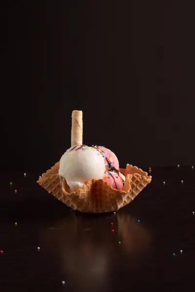 Vanilyalı ve çilekli dondurma bir kurabiye bardağında servis edilir, waffle külahı ve renkli şekerlerle süslenir..