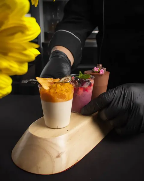 Siyah eldiven giyen bir şef üç farklı tatlıyı kırsal bir ahşap kasede servis eder. Mutfak ve yemek sunumu temaları için mükemmel.