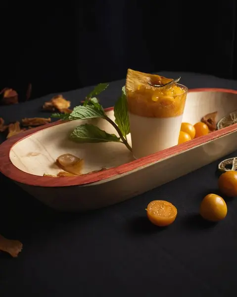 Uchuva tatlısı vanilya kremalı bir bardakta servis edilir, güzel bir şekilde uchuva ile süslenir ve ahşap bir tabakta sunulur. Yemek ve gurme temaları için ideal.