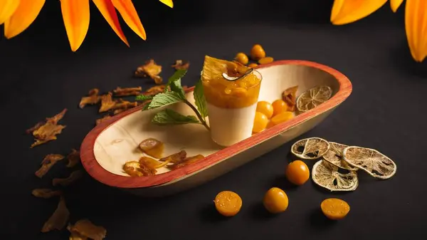 İçinde tatlı olan bir kase bektaşi üzümü. Tatlı, üzerinde yeşil yaprak olan kremalı beyaz bir sos. Kase siyah bir masanın üzerinde.