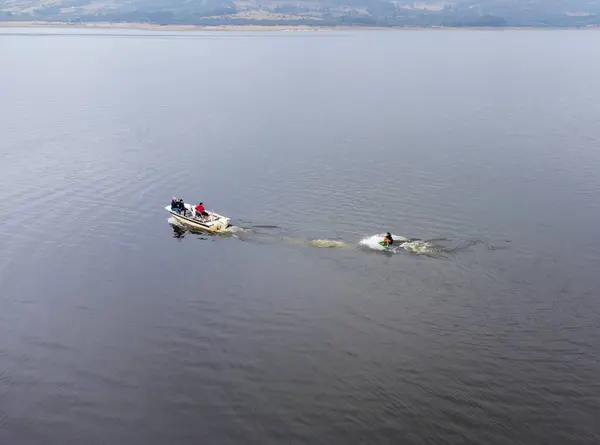 Beyaz bir tekne, sakin sularda sörf yapan birini çekiyor..