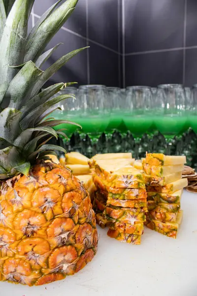 Dilimlenmeye hazır taze bir ananasın yakın çekimi. Meyvenin canlı sarı ve yeşil renkleri çok güzel yeşil içecekler ve arka planda cam örtüler var..