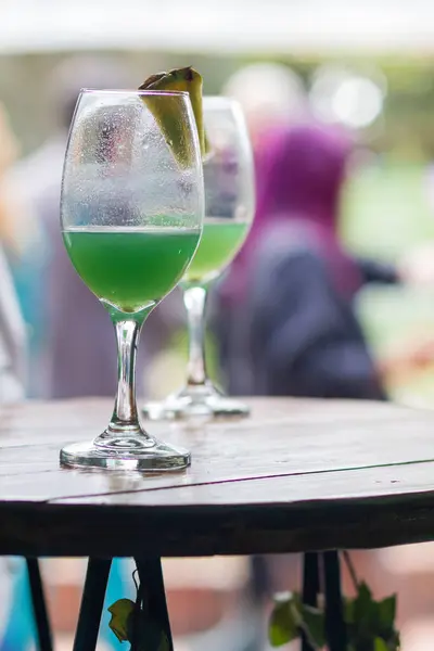 Ahşap bir masada ananas dilimleriyle süslenmiş yeşil kokteyl bardakları, canlı bir etkinlikte çekildi..