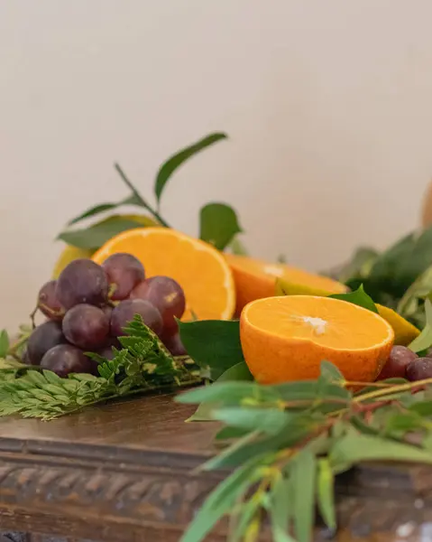Üzüm, portakal ve yeşil yapraklardan oluşan canlı bir düzenleme beyaz bir arka plana karşı ahşap bir masaya yerleştirilmiş, doğal ve taze temalı görseller için mükemmel..