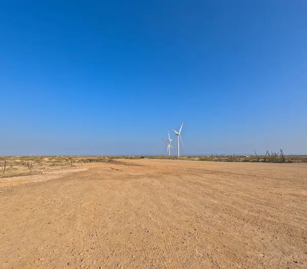 Arka planda açık mavi gökyüzünün altında rüzgâr tarlası olan bir çöl manzarası..