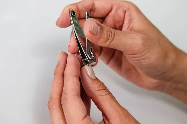 Bir insan tırnaklarını kesmek için metal tırnak makası kullanıyor. Bir elin makası tutarken, diğer elin parmağı tutuyor. Düz arkaplan, basit tırnak bakımına odaklanmayı vurgular..