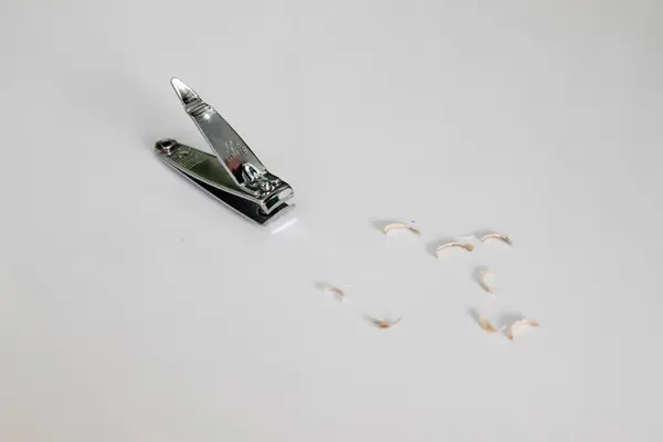 Metal bir tırnak makası, birkaç küçük kesilmiş tırnak parçasının yanına beyaz bir yüzeye yerleştirilir. Arka plan sade ve odak noktası kırpıcı ve yanında düzgün yerleştirilmiş tırnak kesikleri..