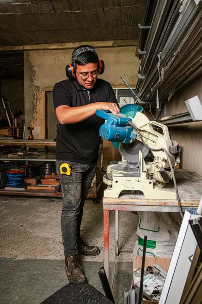 Depoda metal kesme makinesi kullanan, kıvılcımlar saçan bir tüpü dilimleyen bir adam. Otantik endüstriyel atmosfer, üretim ve kalifiye işçilik kavramları için mükemmel.