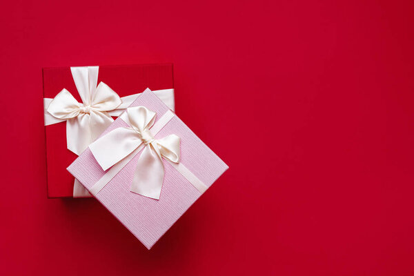 Soft Selective focus on two beautiful gift boxes with satin light ribbon on red background. Pink gift for Christmas, New Year or romantic Valentines Day. Copy space for text.