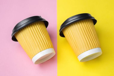 İki sarı kahve ya da çay fincanının yakın çekimi paralel konulmuş ve renkli bir tasarım masası ya da kağıda yatırılmış. Pembe arka plan. Uzayı metin için kopyala. Yumuşak seçici odak