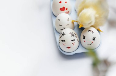 Beautiful hand-painted Easter eggs in a blue tray. Yellow little chicken on eggs on a white background. Minimal concept. Easter card with copy space for text. Soft Selective focus