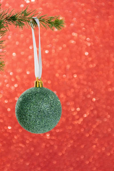 Christmas greeting card. Close-up of green ball toy on Christmas tree branch. Red glowing bokeh background. Minimal style. Copy Space