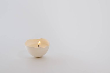 DIY. Easter with your own hands. Candle in eggshell burns on gray background. Yellow light of candle. Copy space