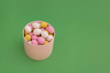 Happy Easter. Chocolate colored eggs in box on a green background. Pink, yellow and white egg colors. Copy Space. Ideal for spring themes, use in marketing materials, packaging.