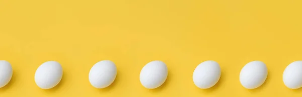 Banner made from White chicken eggs in row on yellow background, top view. Copy Space