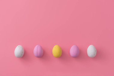 Paskalya kartı. Yumuşak pembe arka planda çok renkli küçük yumurtalar. Şenlikli tatlılar. Boşluğu metin için kopyala. Düz Yat