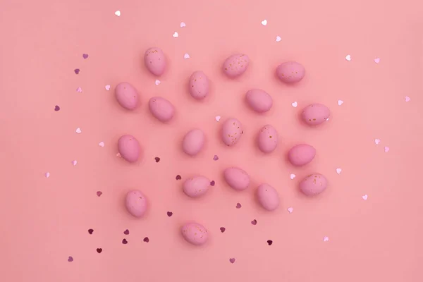 stock image Happy Easter card. Bright pink chocolate eggs lie on pastel pink background. Shimmering glowing hearts. Minimalist composition. Use in marketing materials, decorative element in variety of contexts