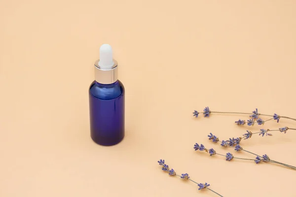 Blue glass dropper bottle with lavender essential oil and dried flowers on beige background. Bottle with metal cap. Serum, cosmetics, massage oil. Copy Space.