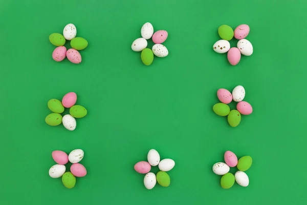 Happy Easter concept. Colorful chocolate eggs arranged in shape of flowers, which form frame on green background. Use for Easter or spring advertising as decorative image for blog. Top view.Copy Space