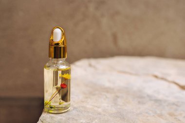 Metal kapaklı cam damlatan şişenin ön görüntüsü ve taş yüzeyinde duran sarı gerekli yağ. Şişedeki küçük çiçekler. Eko krem, serum, kozmetik ürünler, masaj yağı. Kolajen. Boşluğu kopyala