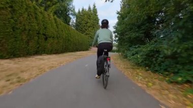 Modern şehir banliyölerinde bisiklet süren bir kadın var. Günbatımı Gökyüzü. Surrey, Vancouver, British Columbia, Kanada. Yavaş Hareket