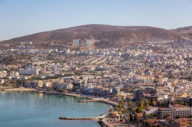 Ege Denizi kıyısındaki bir turistik kasabadaki evler ve binalar. Kusadasi, Türkiye. Güneşli Sabah Gündoğumu. Tepenin Tepesi.