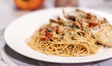 Dinner plate on the table. Gourmet Pasta with sause and sundried tomatoes. Chicken on the side.