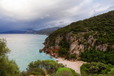 Sandy Beach on a rocky coast near Cala Gonone, Sardinia. Cloudy Sunrise Sky.