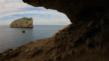 Cave on Rocky Coast with Cliffs on the Mediterranean Sea. Cloudy Sky. Regional Natural Park of Porto Conte, Sardinia, Italy. Nature Background. Slow Motion Cinematic
