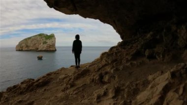 Adventurous Woman in a Cave on Rocky Coast with Cliffs on the Mediterranean Sea. Regional Natural Park of Porto Conte, Sardinia, Italy. Adventure Travel. Slow Motion Cinematic