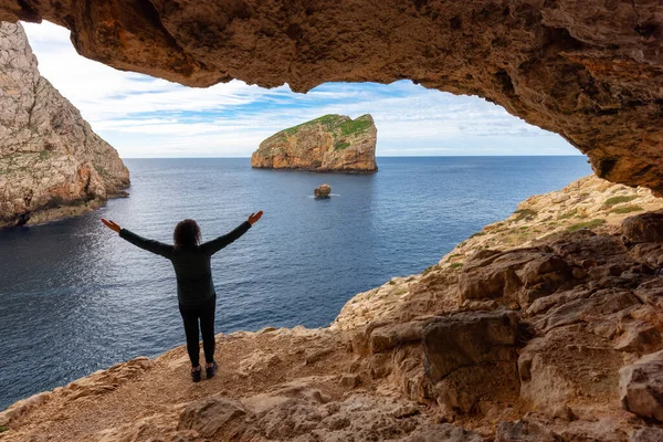 Adventurous Woman in a Cave on Rocky Coast with Cliffs on the Mediterranean Sea. Regional Natural Park of Porto Conte, Sardinia, Italy. Adventure Travel