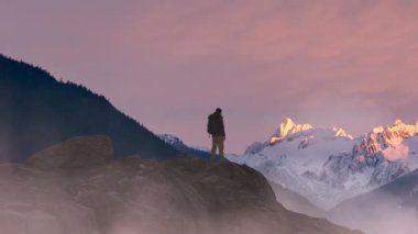 Adventurous Man Hiker standing on top of icy peak with rocky mountains in background. Adventure Composite. 3d Rendering rocks. Image of landscape from BC, Canada. Sunset Sky. 3D Illustration