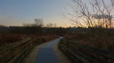 Trail in the modern city, Deer Lake Park. Burnaby, Vancouver, BC, Canada. Colorful Winter Sunset Sky. Slow Motion Cinematic Pan