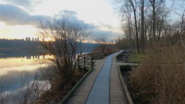 Modern şehir Deer Lake Park 'ta Peaceful Lake' in patikası. Burnaby, Vancouver, BC, Kanada. Renkli Kış Günbatımı Gökyüzü. Slow Motion Sinematik Pan.
