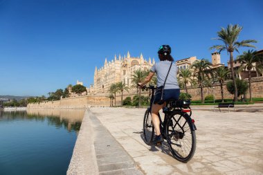 Palma, Balear Adaları 'ndaki Santa Maria de Mallorca Katedral Bazilikası yakınlarında bisiklete binen Maceracı Kadın. Güneşli Gün.