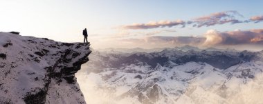 Adventurous Man Hiker standing on top of icy peak with rocky mountains in background. Adventure Composite. 3d Rendering rocks. Aerial Image of landscape from BC, Canada. Dramatic Sky
