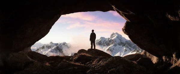 Adventurous Man Hiker standing in a Cave with rocky mountains in background. Adventure Composite. Sunset Sky. 3d Rendering rocks. Aerial Image of landscape from British Columbia, Canada.