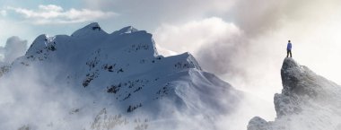 Maceraperest Yürüyüşçü arka planda kayalık dağlarla buzlu zirvenin tepesinde duruyor. Macera Birleşimi. 3D taş kırma. BC, Kanada 'dan havadan görüntü. Günbatımı Gökyüzü. 3B Görüntü