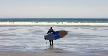 Sörfçü Sörf Dalgaları İçin Okyanusa Doğru Yürüyor. Tofino, BC, Kanada 'daki Vancouver Adası' nın batı kıyısında. Macera Yolculuğu