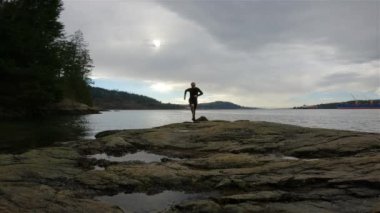 Indian Arm, Vancouver, British Columbia, Kanada 'da Rocky sahilinde koşan Runner Trail. Belcarra, Pasifik Okyanusu 'nun batı kıyısı. Bahar mevsimi güneşli bulutlu bir akşam. Yavaş Hareket