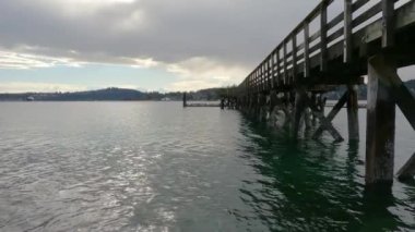 Indian Arm, Vancouver, British Columbia, Kanada 'da kayalık bir sahilde tahta iskele. Belcarra İskelesi, Pasifik Okyanusu 'nun batı kıyısı. Bahar mevsimi güneşli bulutlu bir akşam. Yavaş Hareket