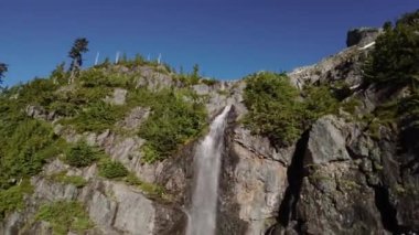 Nehir ve şelale kayalar ve ağaçlarla dağdan aşağı akıyor. Hava Doğası Arkaplanı. British Columbia, Kanada.