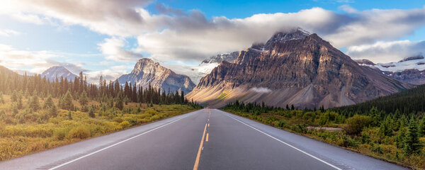 Scenic Road with green trees and Alpine Mountain Peaks in Canadian Nature Landscape. Alberta, Canada.